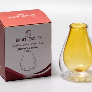 كاسة متة زجاج دبل باللون الأصفر المطفي مع علبة البيت بيتك الحمراء على خلفية بيضاء.